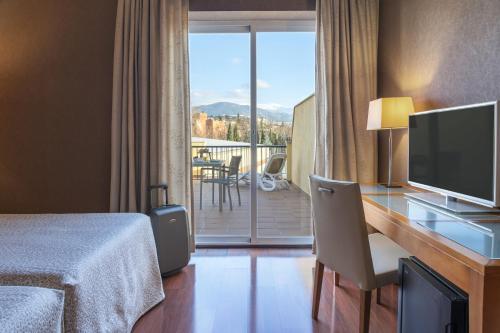 格拉纳达Hotel Macià Monasterio de los Basilios的酒店客房设有一张书桌、一台电视和一个阳台。