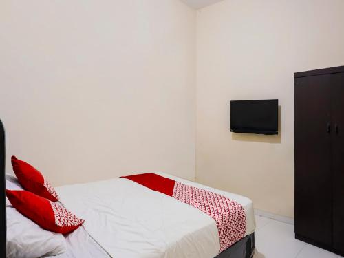 名古屋OYO 92451 Hasan House Syariah 2的一间卧室配有一张带红色枕头的床和一台电视。