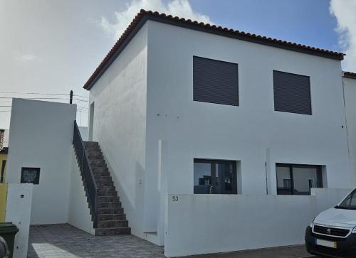 蓬塔德尔加达Casa da Relva的白色的建筑,有楼梯,旁边是汽车