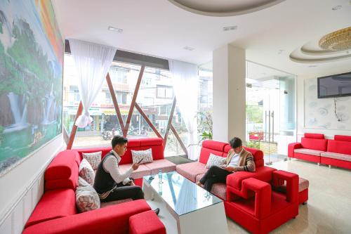 大叻TTR Vincent Hotel的三人坐在客厅里,客厅里摆放着红色的沙发