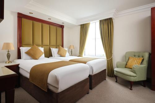 伦敦The Prime London Hotel的酒店客房,配有两张床和椅子
