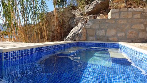 维甘Apartments Kuća Nebeska的蓝色瓷砖游泳池,设有石墙