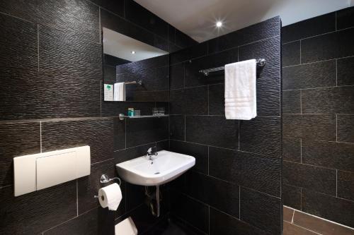 施马伦贝格Parkhotel Schmallenberg的黑色瓷砖浴室设有水槽和镜子