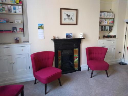 克里基厄斯Tirionfa Guest House的客厅配有2把红色椅子和壁炉