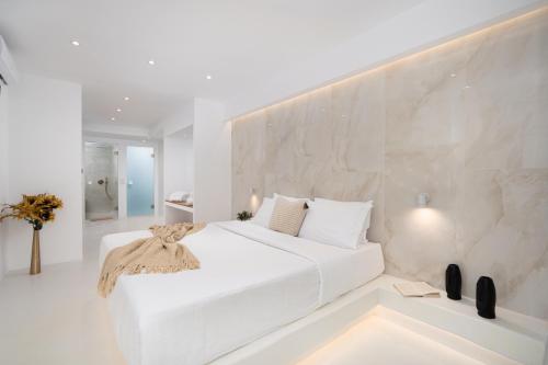 费拉Cycladic Suites的白色的卧室设有白色的床和石墙