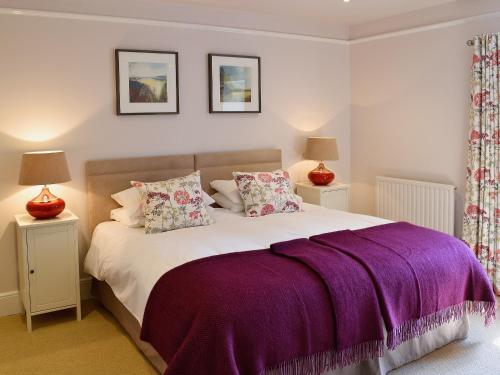 Luxulyan普里多乡村别墅的一间卧室配有一张大床,提供紫色床单和枕头
