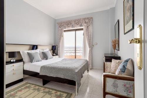 卡帕里卡海岸JOIVY Vibrant flat with balcony的一间卧室设有一张床、一个窗口和一把椅子