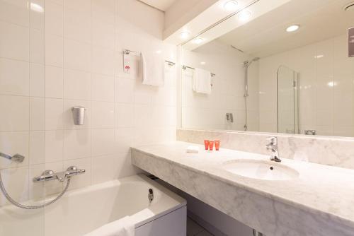 莱利斯塔德Leonardo Hotel Lelystad City Center的一间带水槽、浴缸和镜子的浴室