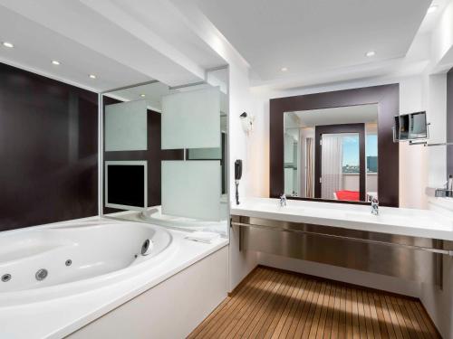布加勒斯特布加勒斯特市中心诺富特酒店的一间带浴缸和大镜子的浴室