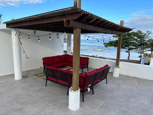 阿瓜达Aguada Beach Condos的露台设有凉亭,配有红色椅子,俯瞰着大海