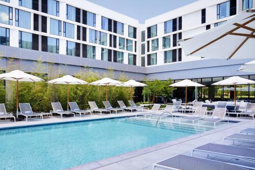 达拉斯AC Hotel By Marriott Dallas By The Galleria的一座带椅子和遮阳伞的游泳池位于一座建筑旁边
