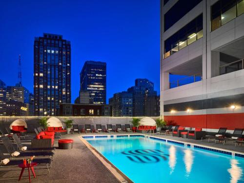 费城Sonesta Philadelphia Rittenhouse Square的夜间酒店带椅子的游泳池以及城市天际线