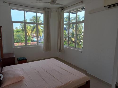 尼甘布The Anchorage Villa - Negombo的一间卧室设有一张床和两个棕榈树窗户。