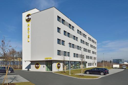 格拉茨B&B Hotel Graz City-Süd的白色的建筑,有汽车停在停车场