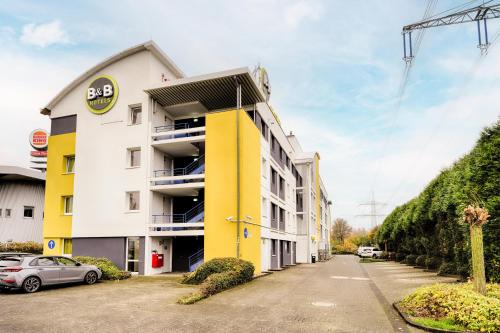 弗雷兴B&B HOTEL Köln-Frechen的一座黄色和白色的建筑,外面有停车位