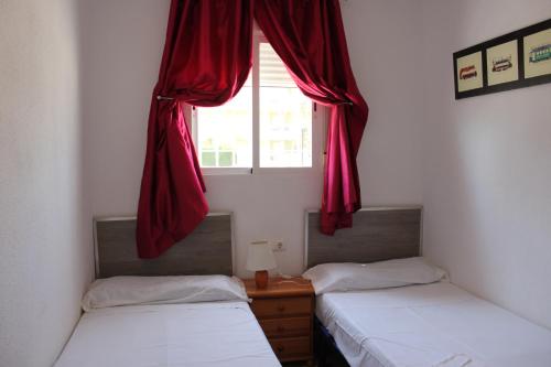 普拉亚西拉科Delfines II Solo Familias Serviplaya的宿舍间的两张床,配有带红色窗帘的窗户