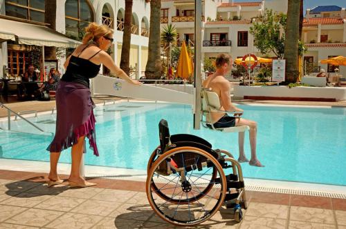 阿罗纳Spa & Sport Hotel Mar y Sol的游泳池附近的一个女人和一个男人坐在轮椅上
