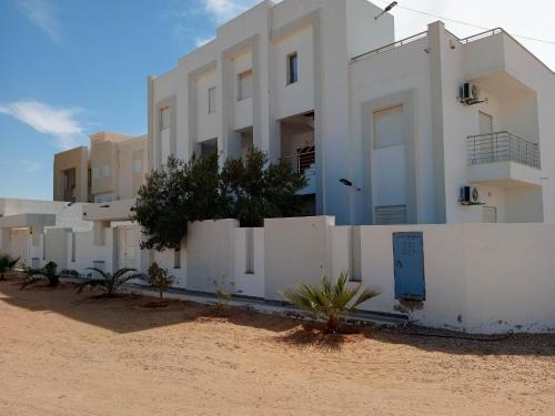 乌姆苏克Résidence Inès Djerba Appartement de Luxe的海滩上一座白色的建筑,靠近围栏