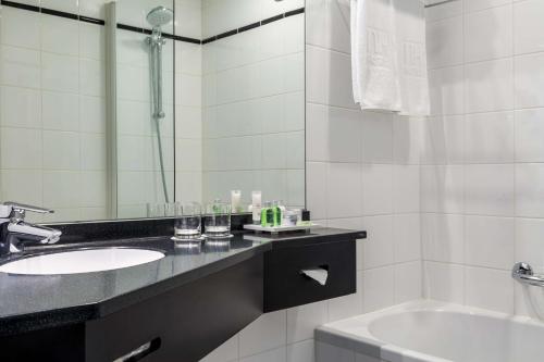 鹿特丹鹿特丹亚特兰大NH酒店的浴室配有盥洗盆、镜子和浴缸