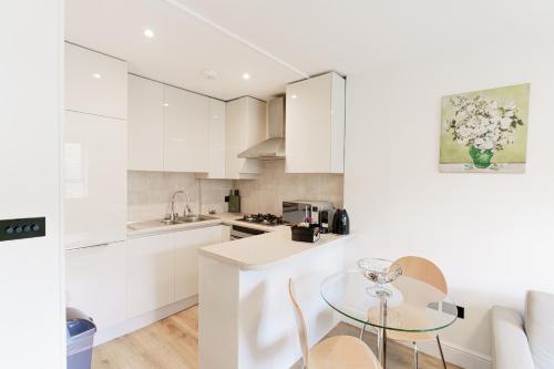 伦敦Penywern Apartment Earls Court的厨房配有白色橱柜和玻璃桌