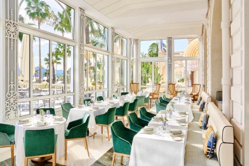 戛纳Carlton Cannes, a Regent Hotel的餐厅设有白色桌子和绿色椅子及窗户