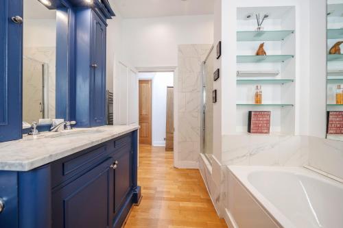 伦敦Luxurious Mews House Next to Hyde Park的浴室设有蓝色橱柜、浴缸和水槽。
