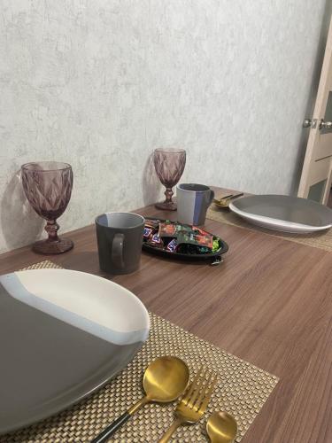 库斯塔奈Комфортабельные - уютные апартаменты в Костанай мкр Береке1的木桌,带盘子、玻璃杯和勺子