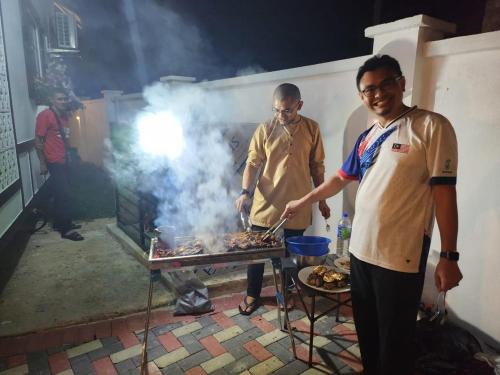 Kampong Bari KechilBERUNTUNG KE BARI RESORT @ PANTAI PENARIK的两个男人在烤架上做饭