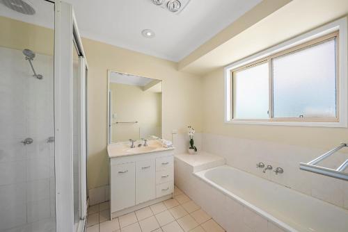 黄金海岸Pet Friendly Family Home with Pool Close to Theme Parks的白色的浴室设有浴缸、水槽和镜子