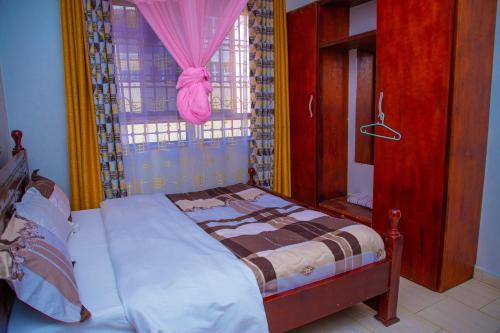 MbaleJ & A VILLAS的一间卧室配有床和一个带粉红色窗帘的窗户。