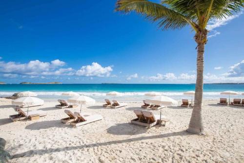 东方湾Casa Del Mar, luxury and magical view of Orient Bay的海滩上摆放着椅子和遮阳伞,还有棕榈树