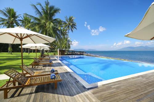 外南梦Villa SoLong Banyuwangi的毗邻大海的带椅子和遮阳伞的游泳池