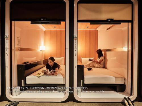 大阪First Cabin Nishi Umeda的两人坐在房间里的床边