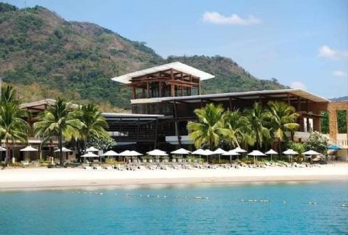 CutadPico De Loro Hamilo Coast beach and Country Club - Myna B One Bedroom的海滩上的度假村,配有椅子和遮阳伞