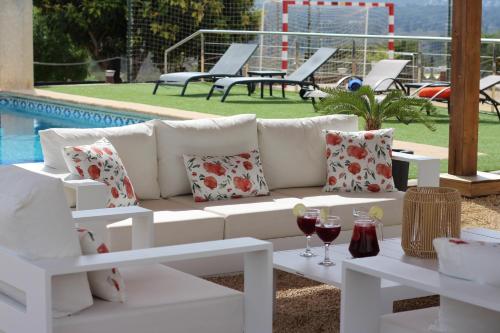 哈维亚Casa Rancho Grande的一张白色沙发,坐在游泳池旁,配上一杯葡萄酒