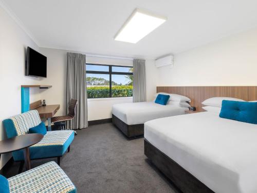 汉密尔顿JetPark Hamilton Airport New Zealand的酒店客房带两张床和一张桌子以及椅子。