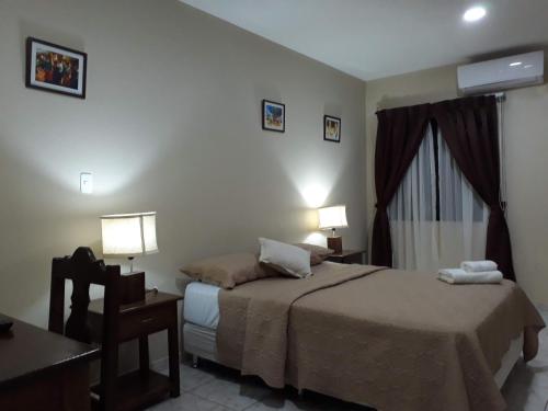 San José de ChiquitosEl Suto Apart Hotel的一间卧室配有一张床、一张桌子和两盏灯。