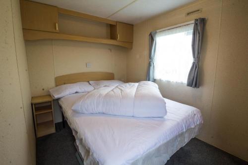 亨斯坦顿6 Berth Caravan For Hire At Manor Park Holiday Park In Norfolk Ref 23025t的一间卧室配有一张带白色床单的床和一扇窗户。