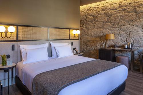 波尔图Hotel das Virtudes的一间卧室设有一张大床和石墙