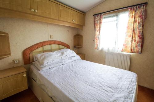 赫彻姆6 Berth Caravan For Hire, Minutes From A Stunning Beach In Norfolk! Ref 21036f的一间卧室配有一张带白色床单的床和一扇窗户。