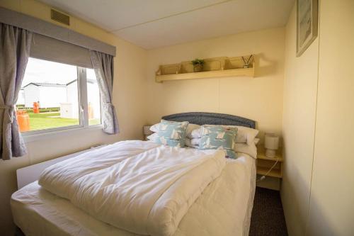 亨斯坦顿Caravan With Decking At Manor Park, Nearby Hunstanton Beach Ref 23013c的卧室配有带枕头的床铺和窗户。
