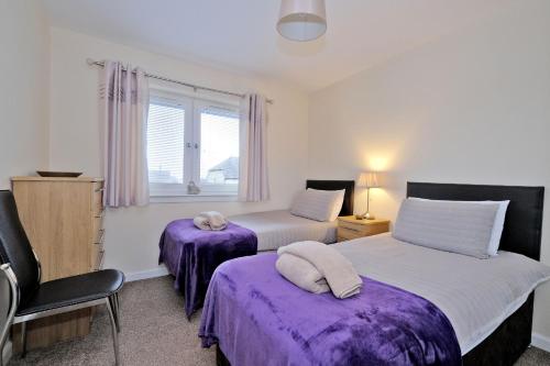 阿伯丁Caledonia Newhills Apartment的一间卧室设有两张带紫色床单的床和窗户。
