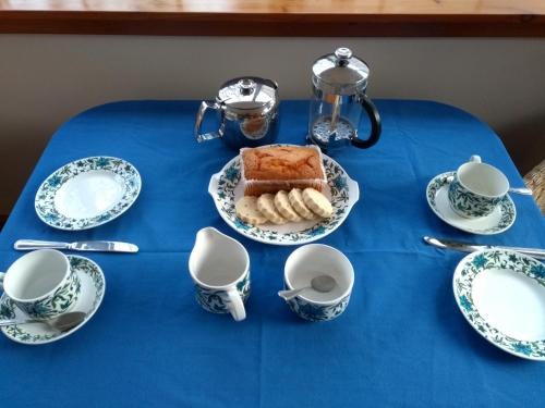 班科里Bridge of Bennie Cottage的一张桌子,上面有蓝桌布,上面有蛋糕和杯子