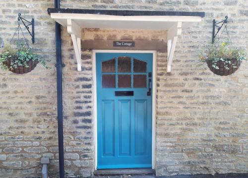 LuckingtonCotswold Cottage Bed & Breakfast的砖楼里一扇蓝色的门,两棵盆栽植物