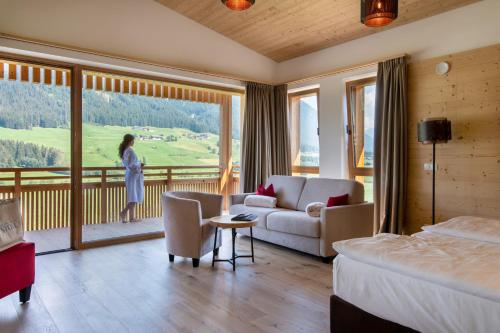 瓦莱迪卡谢斯Alpine Nature Hotel Stoll的一间酒店客房,配有一张床,一名女士站在阳台上