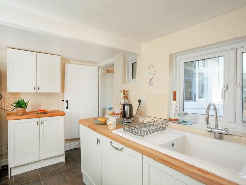 奥特里圣玛丽Otters Cottage的厨房配有白色橱柜、水槽和窗户。