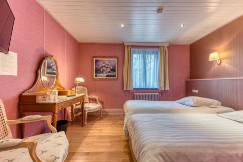 圣胡伯特Hôtel Le Cor de Chasse的酒店客房设有两张床、一张桌子和一面镜子