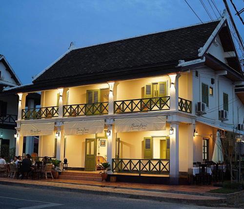 琅勃拉邦Barn Laos Luangprabang Hostel的一座白房子,前面有坐在桌子上的人