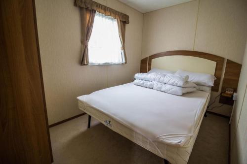 劳斯8 Berth Caravan With Decking At Sunnydale In Lincolnshire Ref 35087s的一间卧室配有带白色床单和枕头的床。