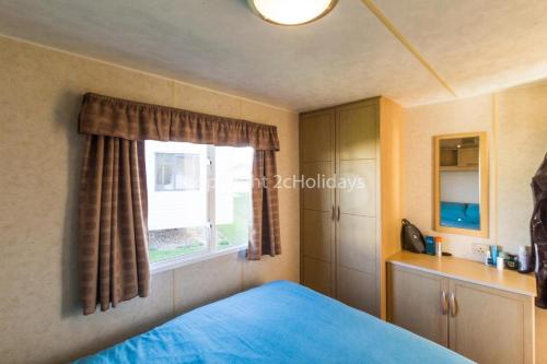 劳斯Great 6 Berth Caravan For Hire At Sunnydale Holiday Park In Skegness Ref 35150tm的一间卧室设有蓝色的床和窗户。